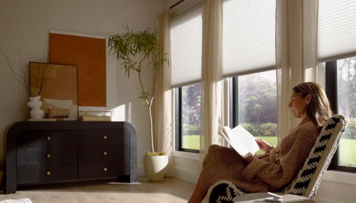 A woman reads a book at home in front of her luxury shades.