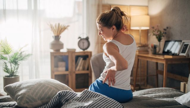 View from behind of a woman holding her back after getting out of bed