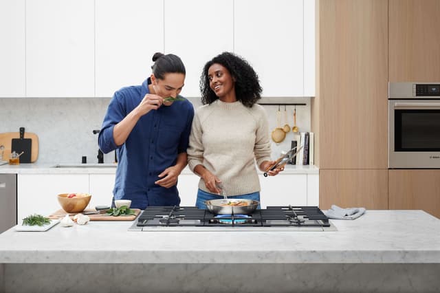 Front view of a couple cooking in a casual kitchen on a Bosch gas cooktop Front view of a couple cooking in a casual kitchen on a Bosch gas cooktop