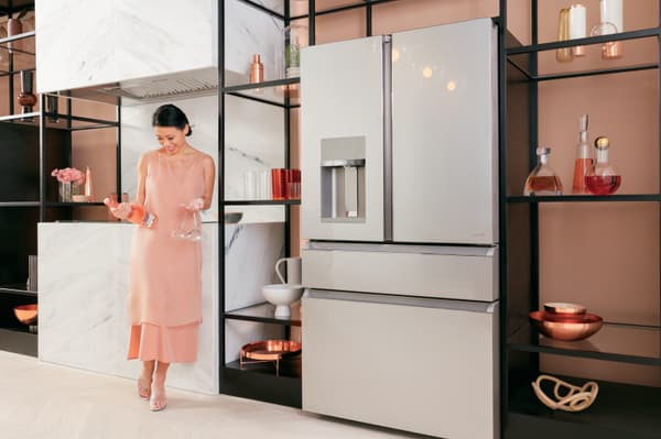 Woman holds bottle of Rose and wine glasses next to her French door refrigerator