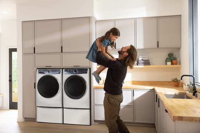 Front view of a modern laundry room with an Electrolux washer and dryer and a man lifting his daughter in the air
