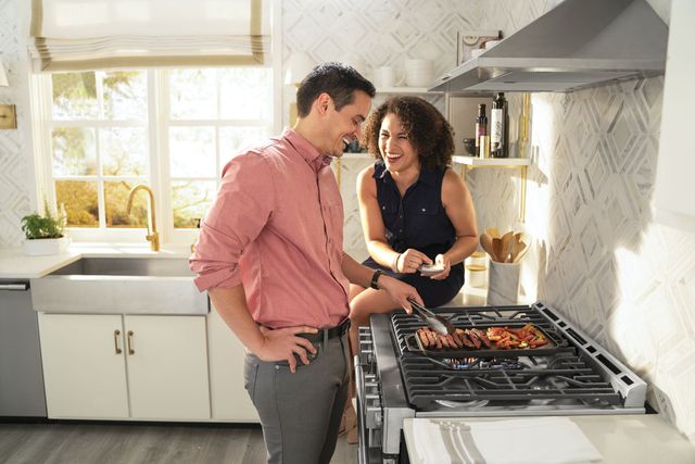 Credit: Frigidaire Professional Side view of couple cooking on a Frigidaire Professional range with a range hood above