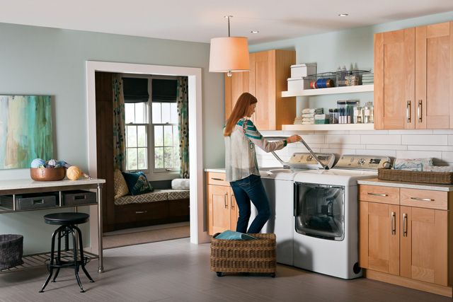 View of a modern laundry room as a woman stands and uses her GE top load washing machine.