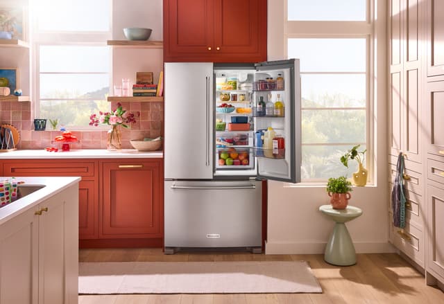 Front view of a modern kitchen with a KitchenAid french door refrigerator with one door open