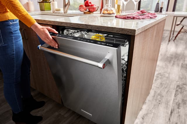 Credit: KitchenAid Front view of a woman closing her stainless steel KitchenAid dishwasher