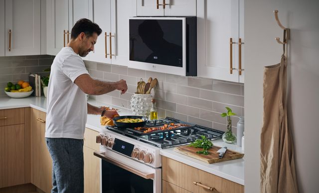 Front view of a man cooking on an LG range with a matching LG over the range microwave