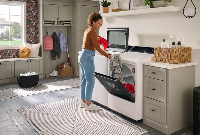 Front view of a woman moving clothes from an LG top load washer to dryer
