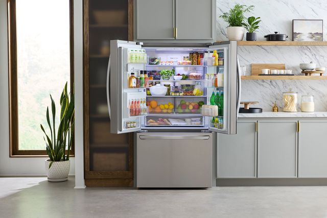 Front view of a modern kitchen with an opened and stocked french door refrigerator 