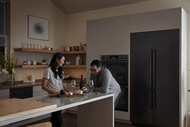 Front view of a couple sharing a glass of wine in modern kitchen in front of luxury Samsung kitchen appliances