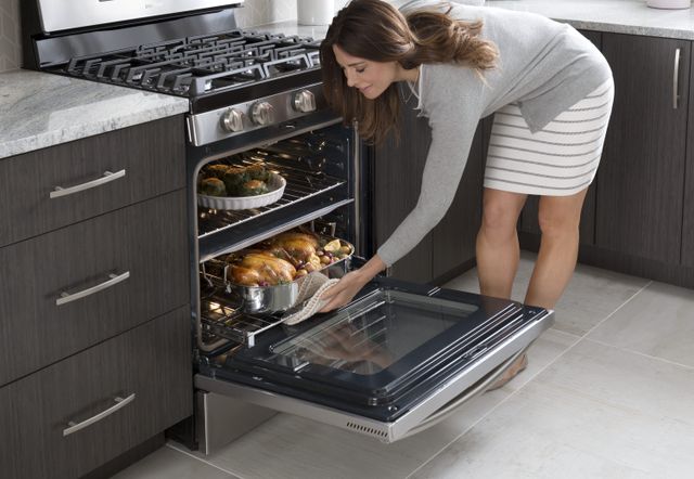 Front view of a woman cooking food in the oven of her gas range in a modern kitchen
