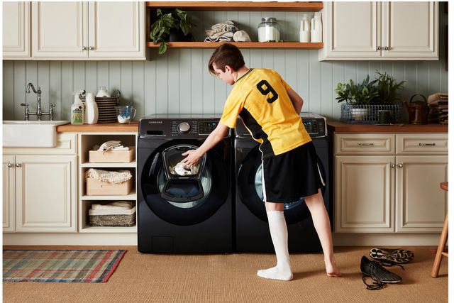 Front view of a modern laundry room with a Samsung washer and dryer, and a child putting their soccer uniform in the washer.