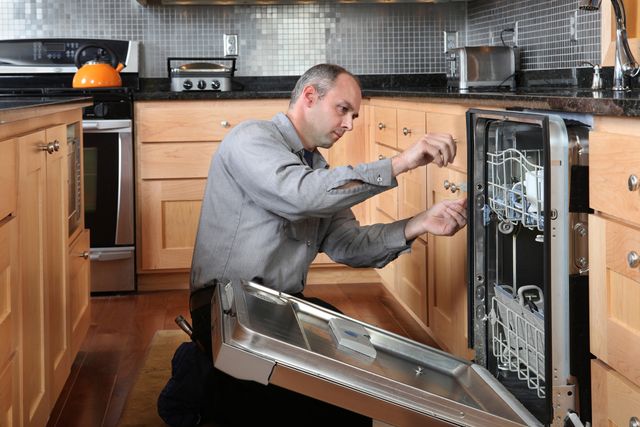 Side view of a man installing a dishwasher in a modern kitchen