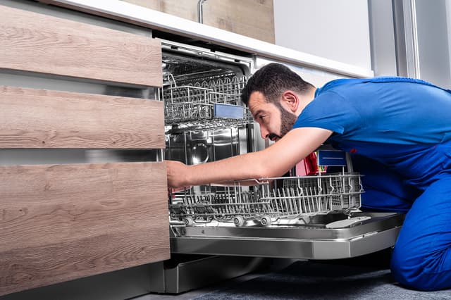 Front view of an installation man reaching into and installing a dishwasher