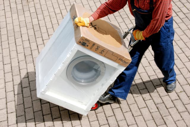 Credit: iStock View of a man wheeling a washing machine in a driveway
