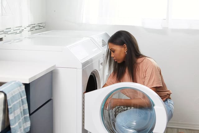 View of a woman kneeling down and looking inside her front load Speed Queen washing machine View of a woman kneeling down and looking inside her front load Speed Queen washing machine