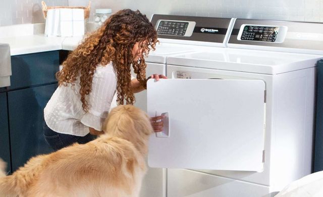 View from behind of a woman and her dog and she kneels down and opens her Speed Queen dryer.