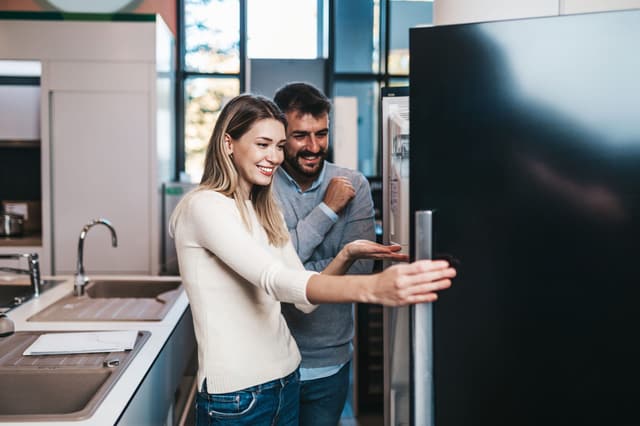View of a couple shopping for a new refrigerator in an appliance store View of a couple shopping for a new refrigerator in an appliance store