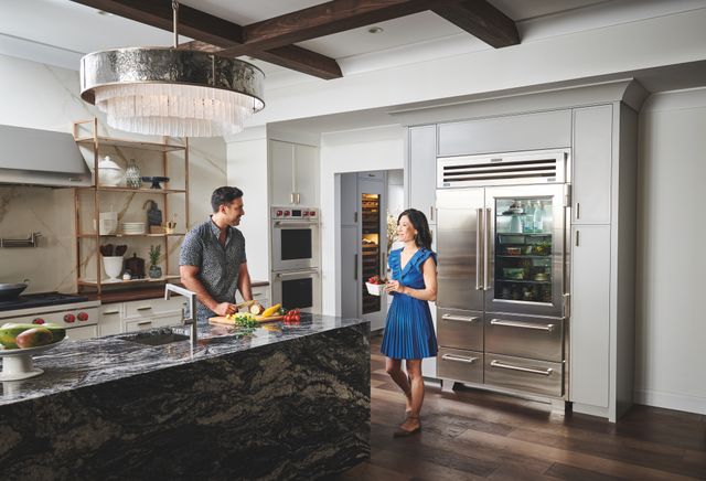 Front view of a modern kitchen with a Sub-Zero refrigerator, as a man and woman cook in the kitchen.