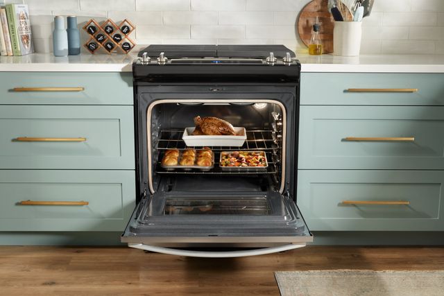 Front view of a gas range with the oven opened and food baking inside