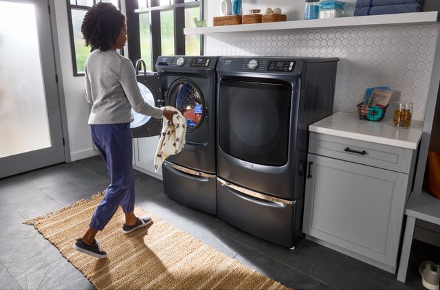Front view of a woman loading clothes into her front load Whirlpool washer and dryer