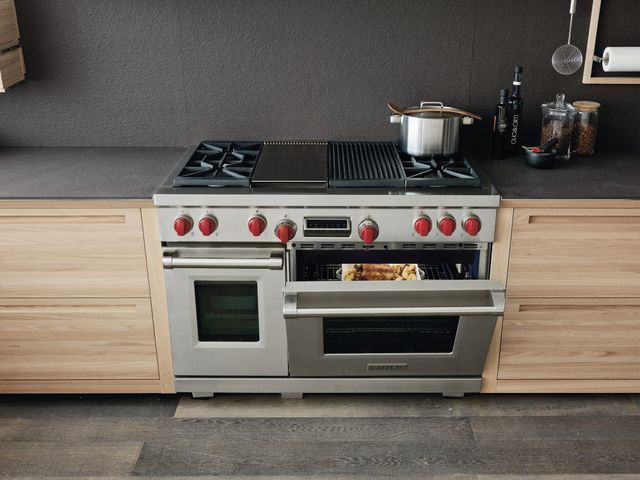 Credit: Wolf Front view of a modern kitchen with an opened Wolf range oven with pots cooking on top.
