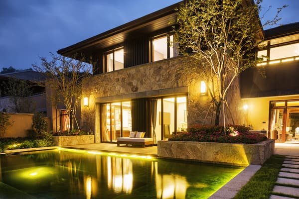 A beautifully illuminated house exterior at dusk, showcasing smart outdoor lighting along the roofline, windows, and landscaping.