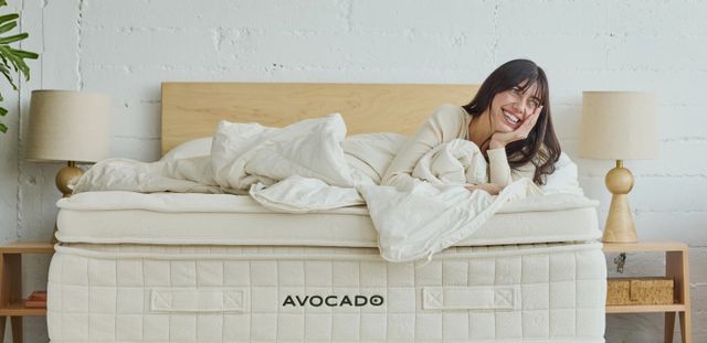 Front view of a modern bedroom with a woman laying comfortably on an Avocado mattress