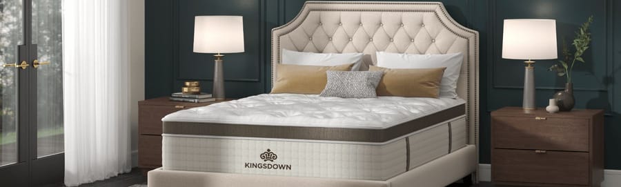 Kingsdown mattress displayed in a styled bedroom with a tufted headboard, nightstands, and bedside lamps.