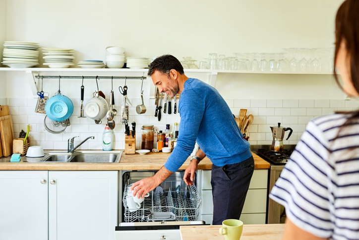 young couple talking in the kitchen and loading the dishwasher