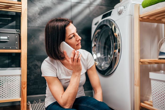 woman in laundry room by washing machine calling appliance repair service