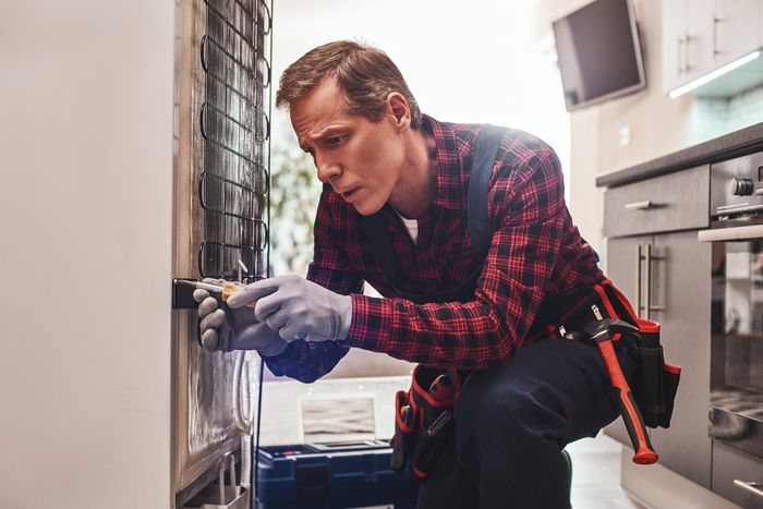repairman uses screwdriver to install new refrigerator