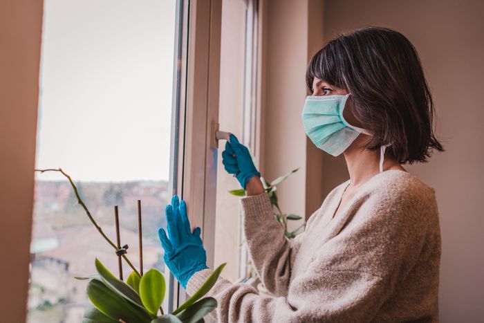 woman wearing medical mask and disposable gloves stares out window 