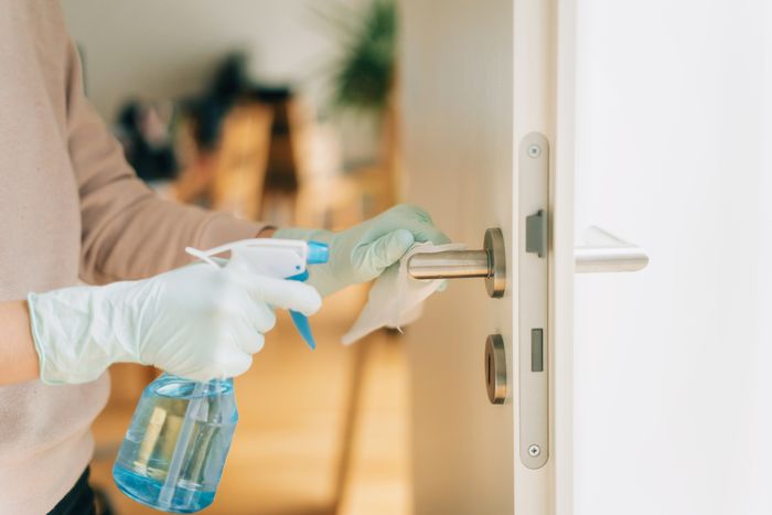 woman in disposable gloves cleaning the door handle with disinfectant spray