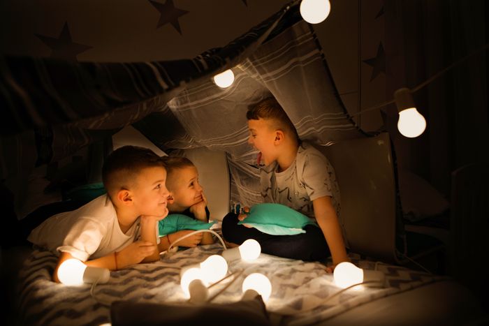 Three young boys playing in blanket fort illuminated by string lights