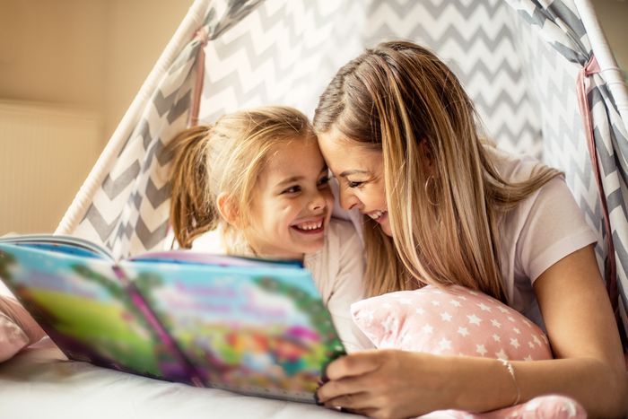 Smiling mother reading a storybook to her young daughter inside a bed tent