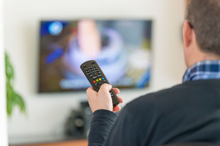dad holding a TV remote changing channels on wall-mounted TV