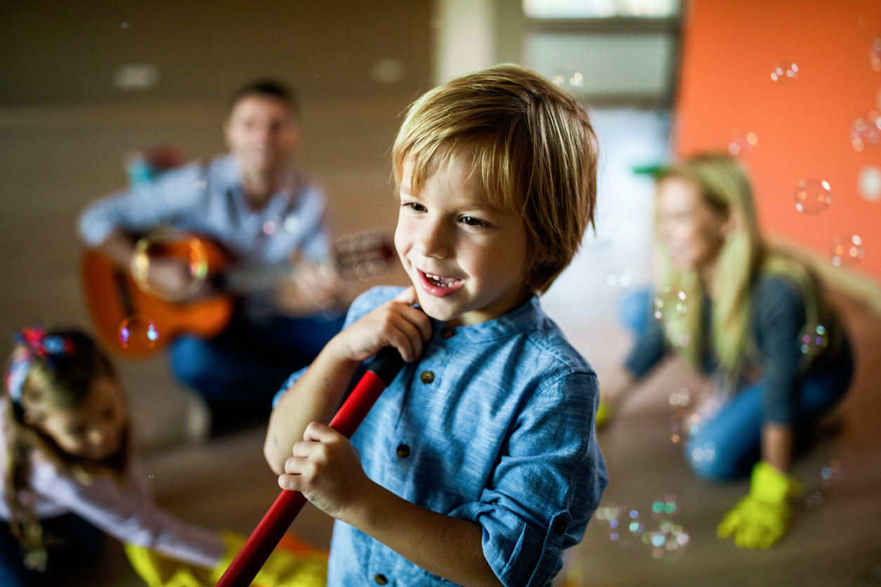 young boy singing with a broomstick in kitchen