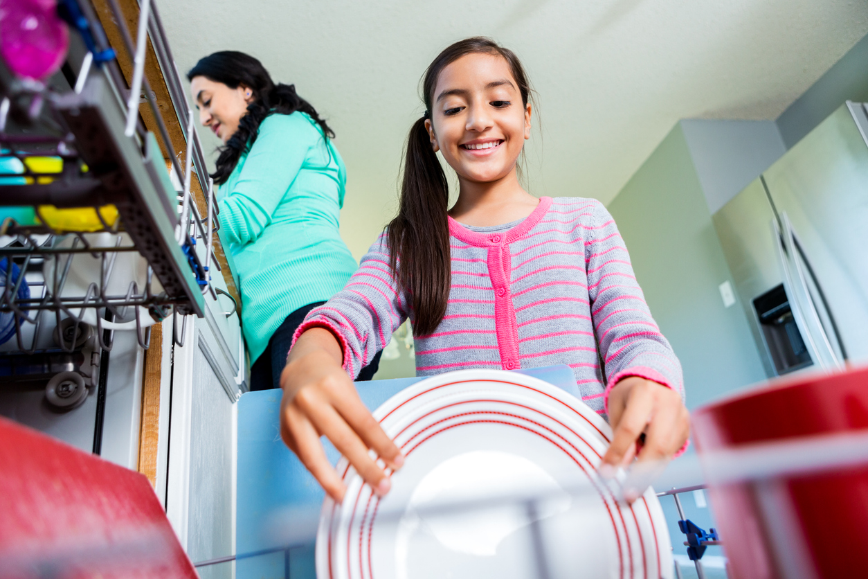 smiling girl loading dishwasher in kitchen