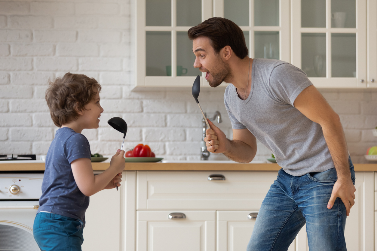 father and young boy singing into spoons in the kitchen