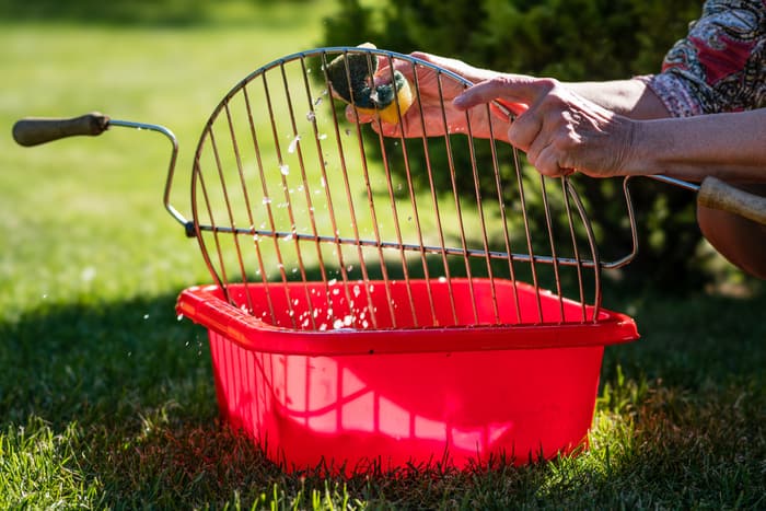removable grill grate is soaked in a tub of water and getting cleaned with a sponge removable grill grate is soaked in a tub of water and getting cleaned with a sponge