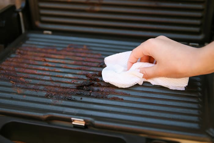 a woman wipes down a dirty electric grill with a cloth a woman wipes down a dirty electric grill with a cloth