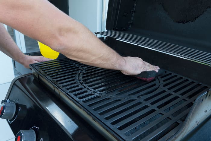 a man wipes down an outdoor gas grill with a sponge a man wipes down an outdoor gas grill with a sponge