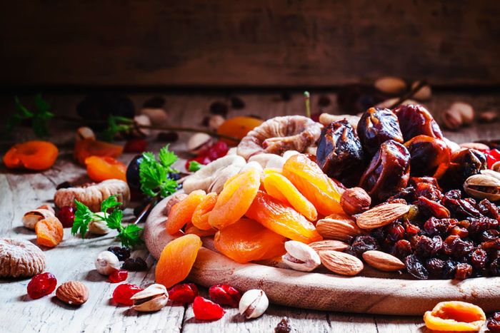 a wooden tray stacked with dried apricots, dates, raisins, and various nuts