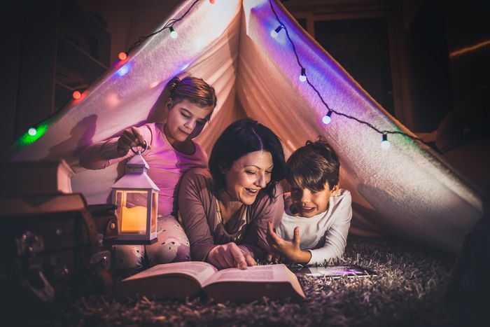 happy mother reads a book to her young son and daughter inside an indoor tent