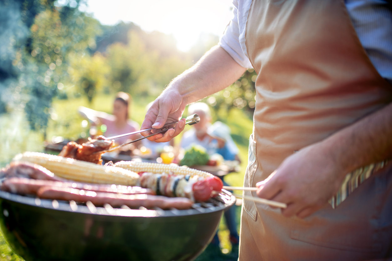 man cooking meat on a free-standing charcoal grill for his family