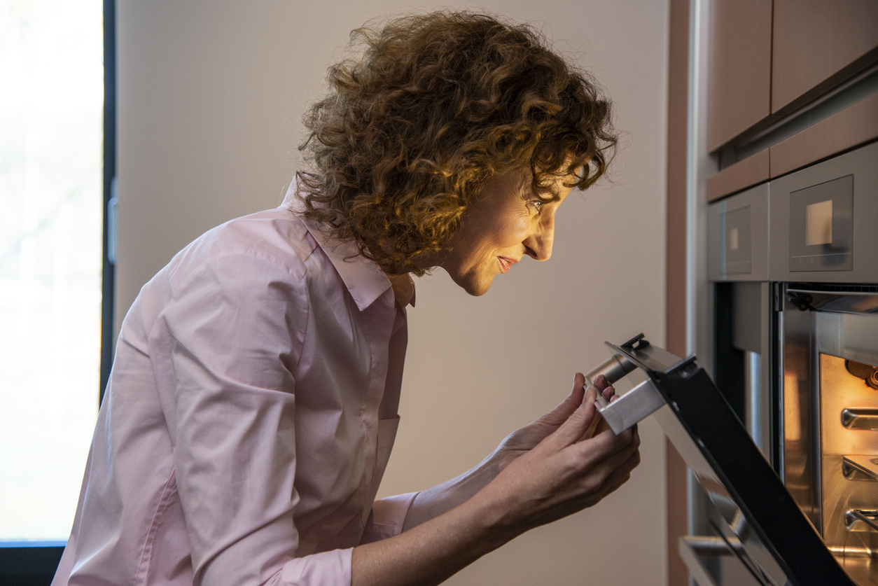 woman opens wall oven to check on her baked goods