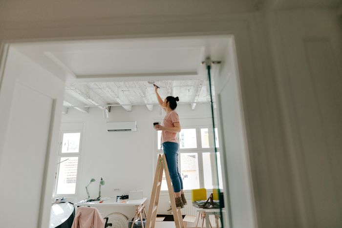 woman on ladder paints ceiling of her modern home office white