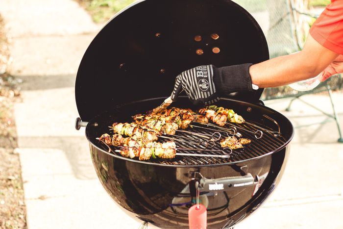 man wearing a grill mitt takes a grill brush over skewers