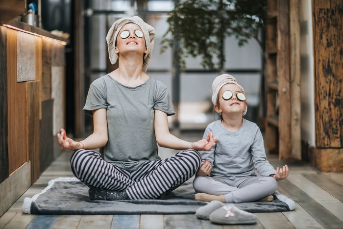 mother and daughter wearing face masks meditate together on the floor