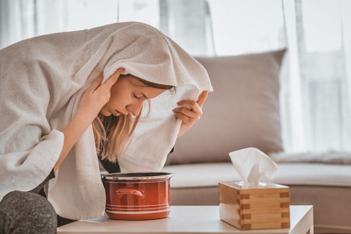 young woman hovers face over a steaming pot with a towel over her head